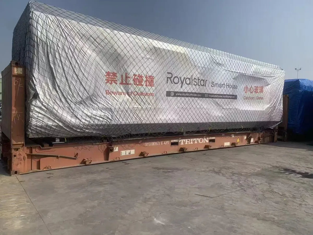 A wrapped cabin strapped to a flat-rack container at the port of loading.